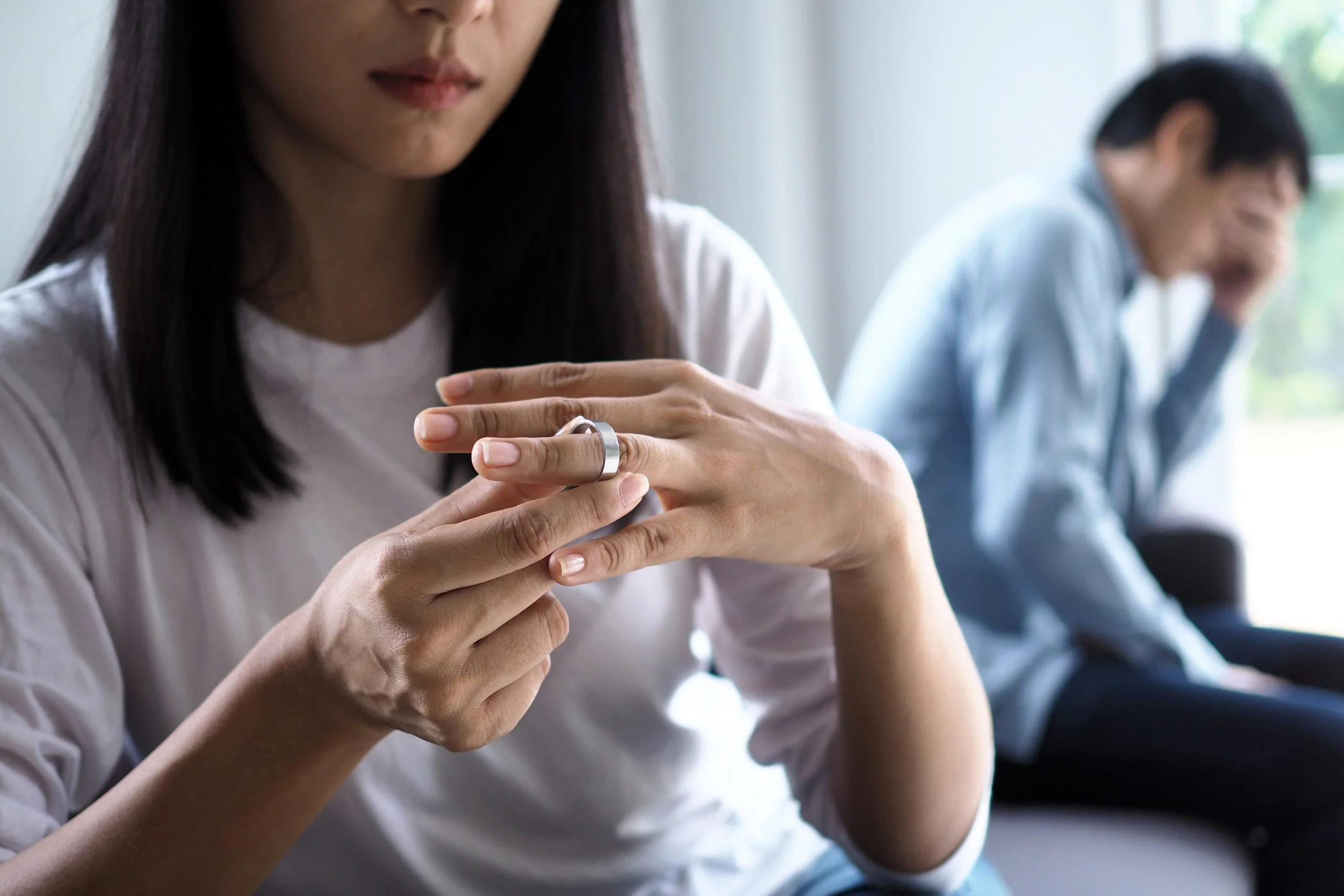 Femme enlevant son alliance avec son mari en arrière plan désappointé
